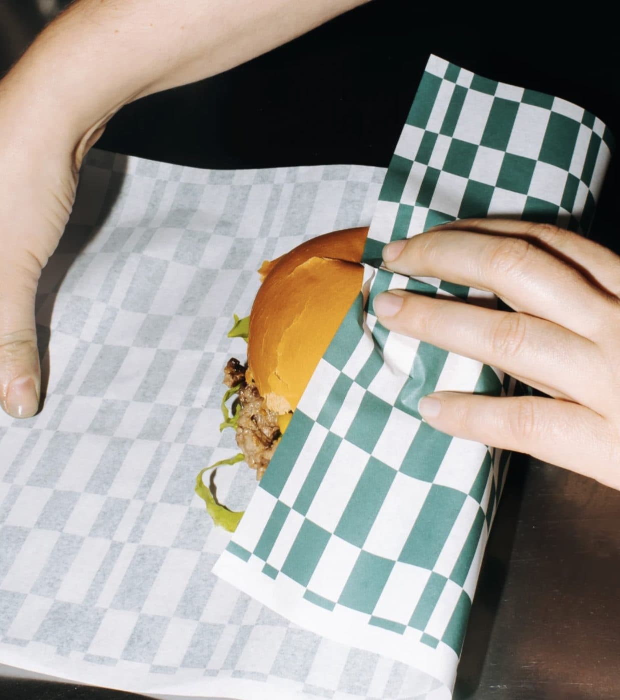 Hands wrapping a burger in printed greaseproof paper